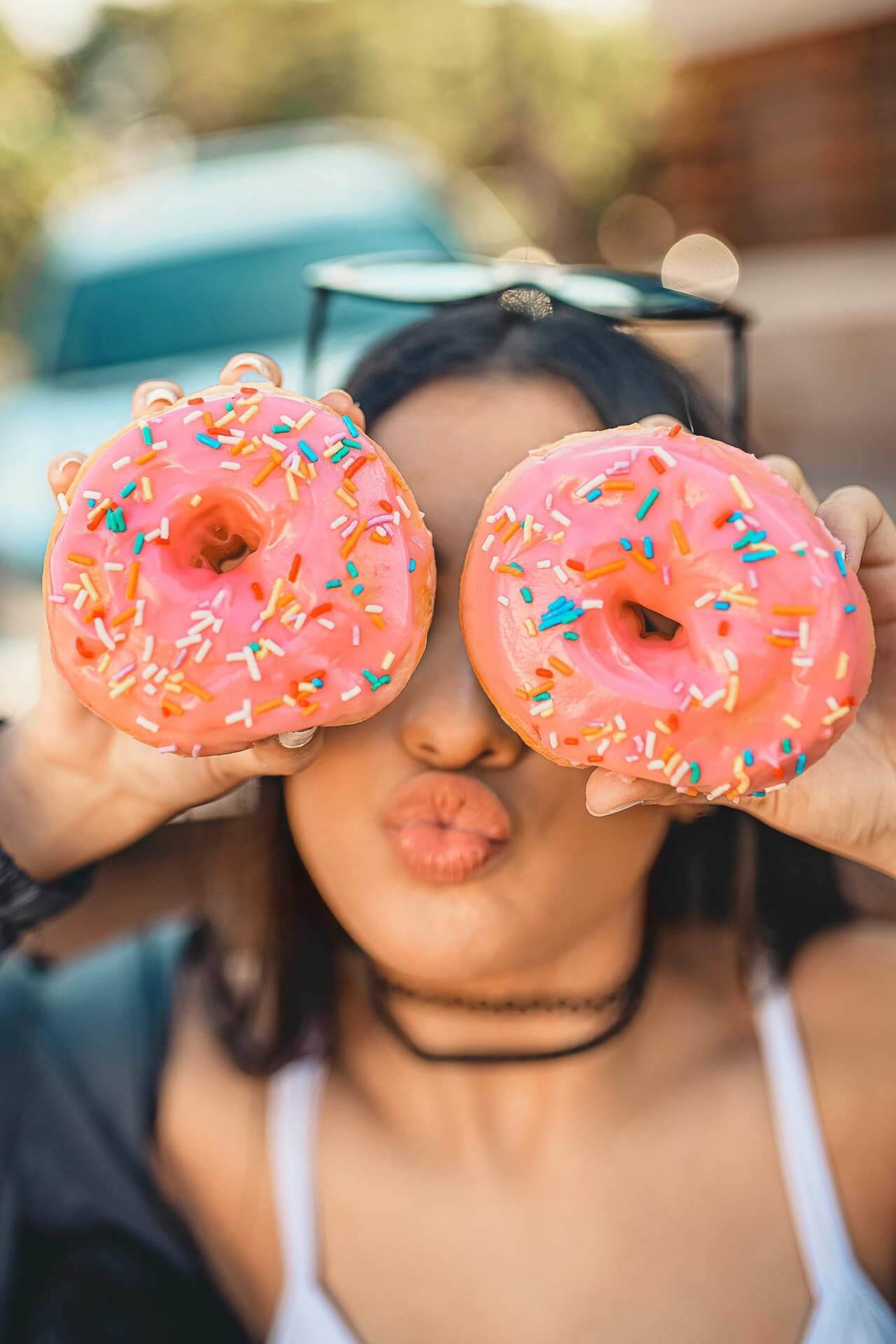 Jovem fazendo bico e colocando dois donuts como se fossem olhos